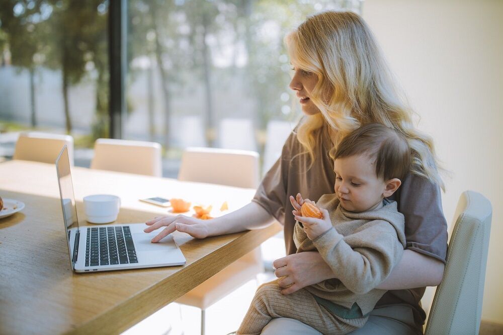 Newly single mom looking for business opportunities on her laptop while holding a baby