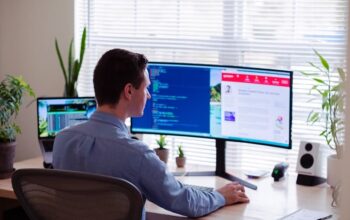 A web developer working at his desk, facing monitors.